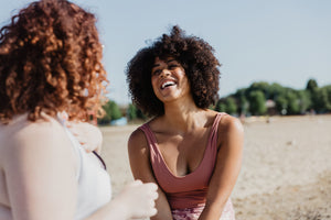 2 young ladies sharing a laugh on the beach. African American girl with natural curly hair displays a vibrant smile 